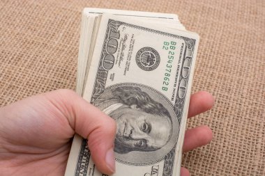 El ele tutuşan bir tomar Amerikan doları keten bir arka planda.