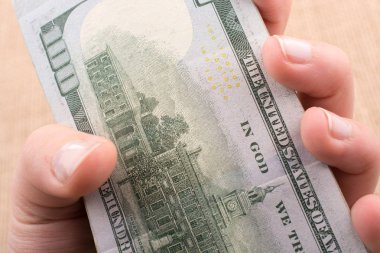 El ele tutuşan bir tomar Amerikan doları keten bir arka planda.