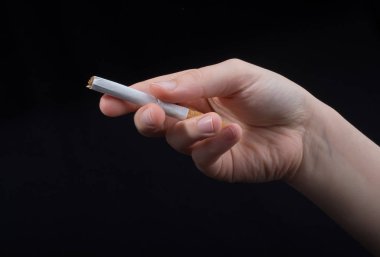 El siyah arka planda bir sigara tutuyor.