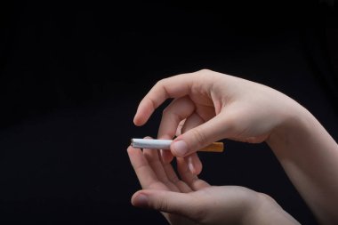 El siyah arka planda bir sigara tutuyor.