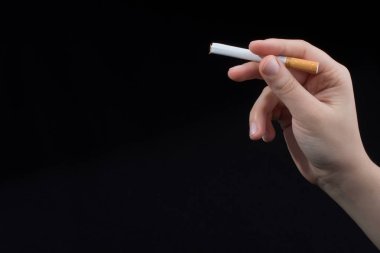 El siyah arka planda bir sigara tutuyor.