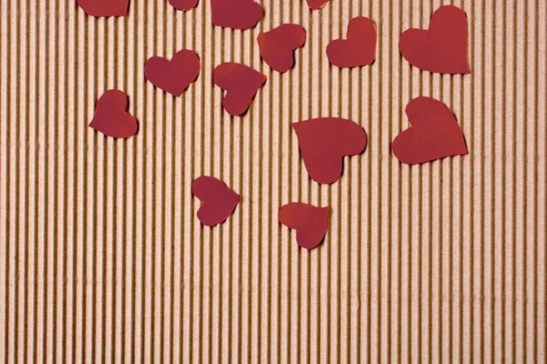 Red color paper hearts on a brown cardboard