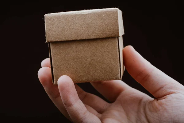 Mão segurando caixa de papelão em um fundo preto — Fotografia de Stock