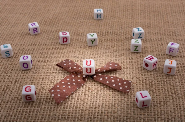 A ribbon and scattered dice-sized alphabet cubes on a textured s — Stock Photo, Image