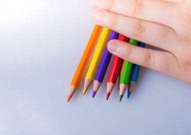 Beyaz arkaplana yerleştirilmiş renkli kalemler tutan kişi