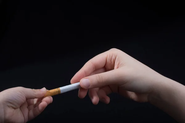 Hand is giving out cigarette on a black background