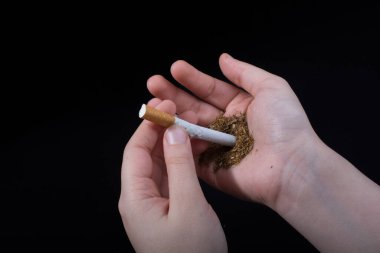 El siyah arka planda bir sigara tutuyor.