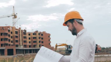 İnşaat sahasında plan ile mühendislik. Kask içinde baş mimar.
