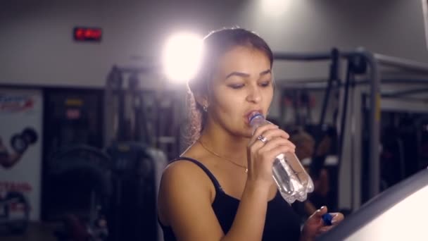 Fitnesssportliches Mädchen trinkt Wasser, das auf einem Laufband in einem Fitnessstudio läuft. — Stockvideo