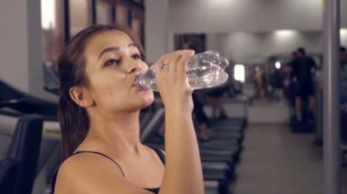 Fitness sportif kız bir spor salonunda bir koşu bandı üzerinde çalışan bir su içme.