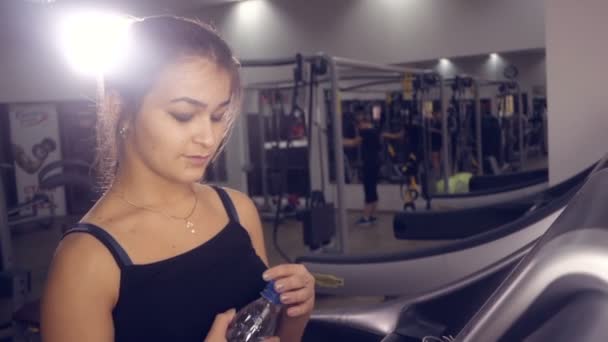 Fitnesssportliches Mädchen trinkt Wasser, das auf einem Laufband in einem Fitnessstudio läuft. — Stockvideo