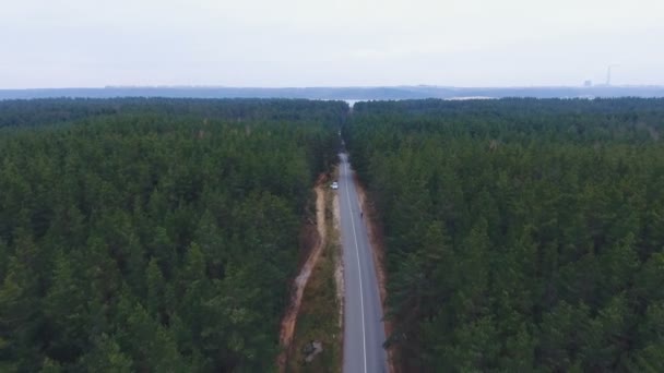 Caméra survolant la route en bois. Forêt dense avec une route avec un homme de course et une voiture sur le bord de la route. D'en haut. Aérien .