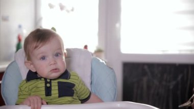 Sevimli gülümseyen bebek yeme, evde Bebek koltuğuna oturuyor. Annesi onu çok güzel bir yıl eski bir kaşıkla besleme.