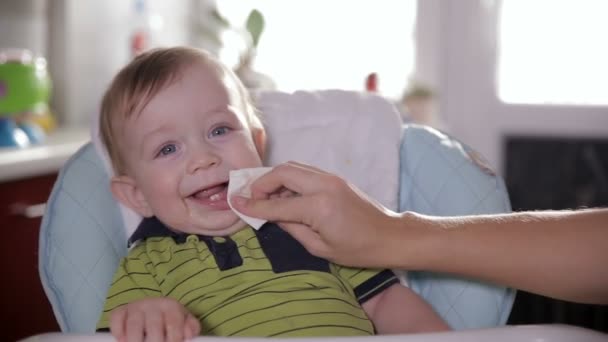 Baby pokryte żywności. Matka pomaga malucha baby do czyszczenia twarzy. Szczęśliwy uśmiechający się ładny dziecko po posiłku. — Wideo stockowe