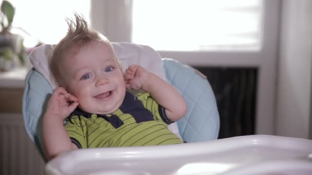 Schattige verlegen baby in een kinderstoel lachen en kijken naar de camera. — Stockvideo