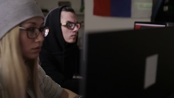 Male and female hackers working on computers with data code on display screens in a dark room. — Stock Video