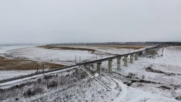 Vista aérea del tren de carga pasa el puente que entrega mercancías, combustible, petróleo en invierno . — Vídeo de stock