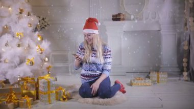 Noel arifesi sırasında Noel ağacının yanında oturan güzel kız kullanım cep telefonu.