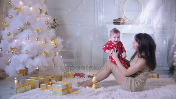 O bebé e a mãe a brincar perto da árvore de Natal. Decoração de ano novo e um conceito de primeiros passos . — Vídeo de Stock