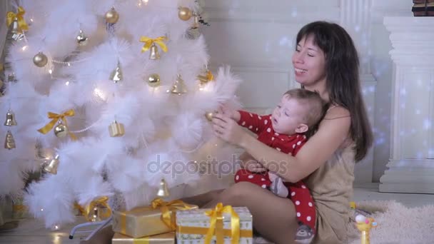 Das kleine Baby und seine Mutter spielen in der Nähe des Weihnachtsbaums. Neujahrsdekoration und ein Konzept für erste Schritte. — Stockvideo