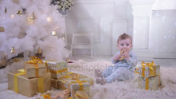 Kind van de baby in de buurt van de kerstboom, bagel eten. — Stockvideo
