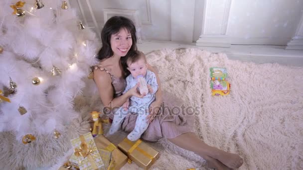 Conceito de família de Natal. Mãe alimentando seu bebê perto da árvore de Natal durante a celebração do ano novo . — Vídeo de Stock