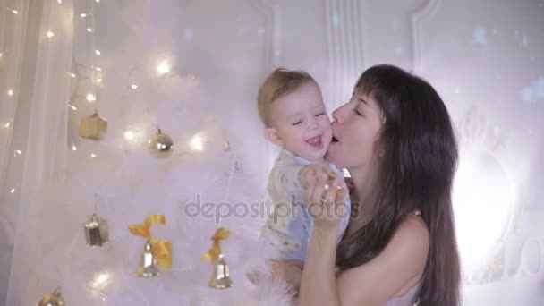 Madre y bebé riendo, divirtiéndose cerca del árbol de año nuevo decorado lleno de luces brillantes coloridas . — Vídeos de Stock