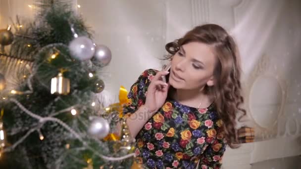 Giovane ragazza carina bello parla dal telefono cellulare vicino all'albero di Natale. Celebrazione di Natale . — Video Stock