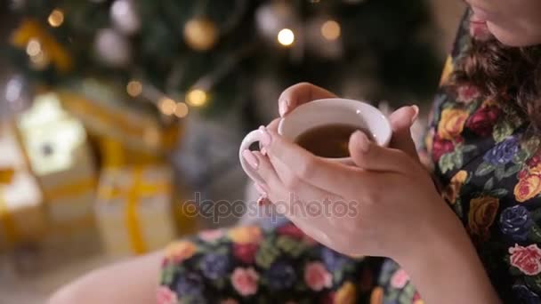 Female hands with tea cup near christmas tree. Beaty girl drinking tea. — Stock Video