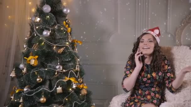 年轻可爱的漂亮女孩说话靠手机附近的圣诞树。圣诞节的庆祝活动. — 图库视频影像