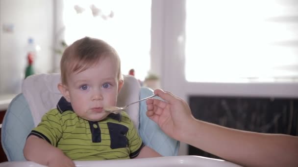 Mutter füttert ungewaschenen Jungen in der heimischen Küche. Kinder und Ernährung. — Stockvideo