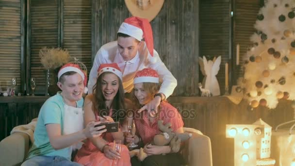 Unbekümmerte Teenie-Freunde feiern Weihnachten in der Nähe geschmückter Weihnachten und betrachten eine neue Anwendung im Smartphone. — Stockvideo