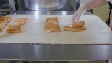 Pasta şefi el koyarak eklerleri, tatlılar bir üretim hattı üzerinde. Konveyör hattı eklerleri hareketli.