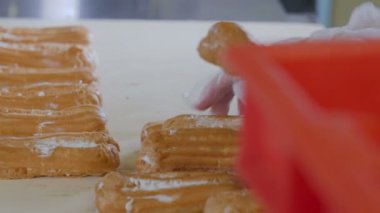 Pasta şefi el koyarak eklerleri, tatlılar bir üretim hattı üzerinde. Konveyör hattı eklerleri hareketli.