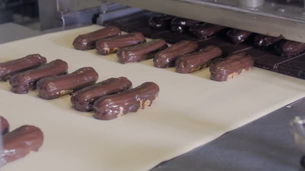 Конвейерная линия с движущимися шоколадными эклерами. Эклеры, торты, кондитерские изделия, линия по производству десертов . — стоковое видео