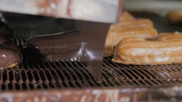 Gesmolten chocolade stroomt op verse romige éclair taarten op een transportband in een bakkerij. — Stockvideo