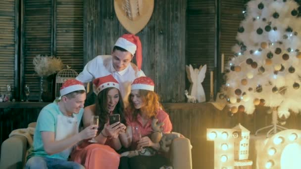 Groep mensen, vrienden met behulp van smartphone in de buurt van versierde kerstboom. — Stockvideo