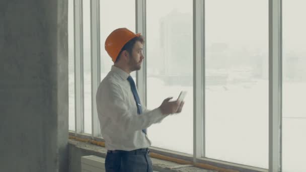 Mestre construtor, empresário de chapéu duro dentro de um canteiro de obras inspecionando o progresso da construção usando tablet. Disparar deslizante . — Vídeo de Stock