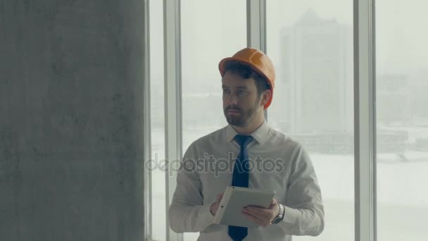 Stavitel, podnikatel v čepice uvnitř staveniště, Kontrola průběhu výstavby pomocí tabletu. Jezdec natáčení. — Stock video