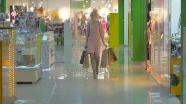 Alışveriş torbaları ile alışveriş merkezinde yürüyen genç kadın.