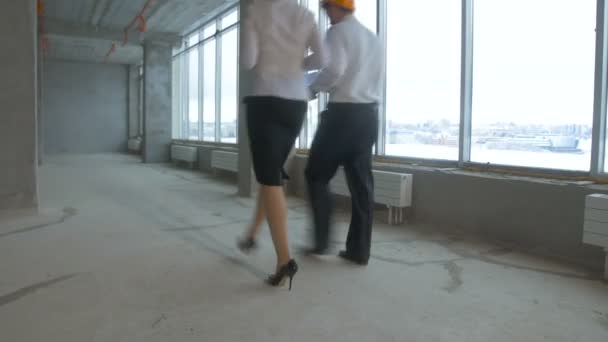 Unrecognizable business team, engineers, realtors in suits working on a construction site, unfinished building. From behind. Steadycam shot. — Stock Video