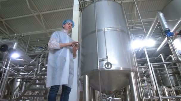 Trabajador en cervecería cerca de tanques, tubería de trabajo con tableta . — Vídeos de Stock
