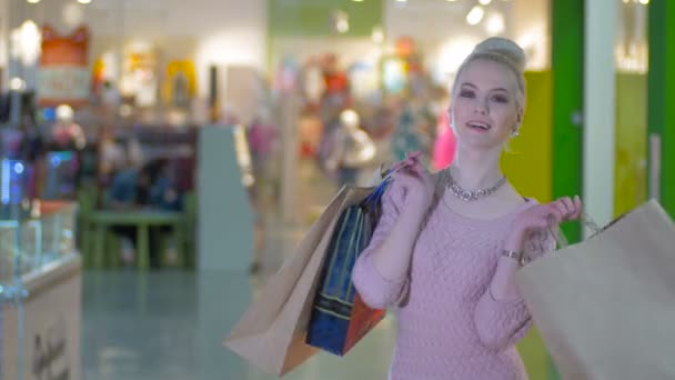 Hermosa chica con bolsas de compras posando, coqueteando en el centro comercial . — Vídeos de Stock