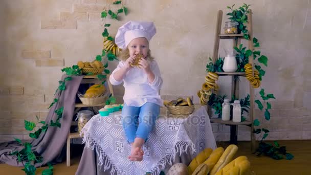 Piccola cuoca carina seduta in cucina sorridente, che gioca con il cibo . — Video Stock
