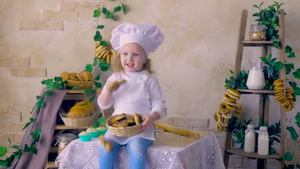 Niña cocinera lanza magdalenas, sentado en la cocina . — Vídeo de stock