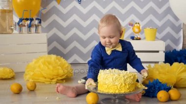 Ellerini kullanarak pasta yemeye küçük bir çocuk. Bir odada doğum günü partisi sırasında karışıklık.