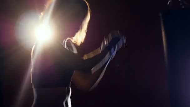 Νεαρή γυναίκα που εγκιβωτίζει στο σκοτάδι. Γυναικεία σιλουέτα κάνοντας shadowboxing. Ισχυρό φως πίσω της. — Αρχείο Βίντεο