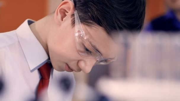 Young school boy mixing liquids in test tube in science class. — Stock Video