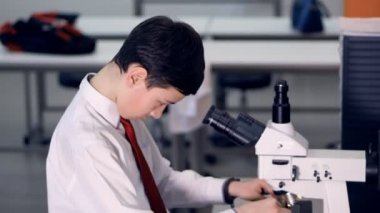 Öğrenci 10-11 yaşında bir okul laboratuvar mikroskop bakarak Biyoloji araştırma yapma.