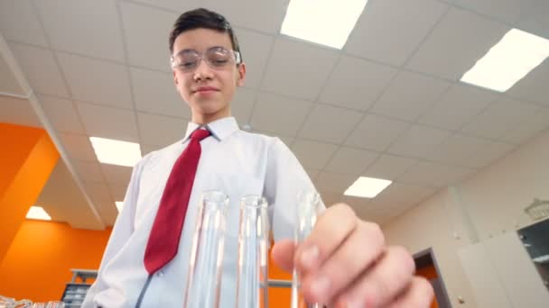 Adolescente en la clase de química de la escuela mirando en el tubo de ensayo, haciendo experimentos . — Vídeos de Stock